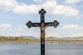 Crucifix - statue of Jesus Christ on a cross, in the background landscape with water, hills and blue sky with clouds Royalty Free Stock Photo