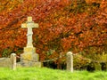 Crucifix stone memorial in chruch grave yard with autumnal leaves on the trees in the background