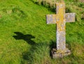 Crucifix stone memorial and shadow in sunlight in church grave yard with autumnal leaves on the trees in the background