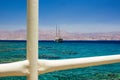 Cruise ship floating on Red sea aquamarine transparent water with coral riffs view on bottom through white fence pipes frame,