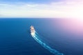 Cruise ship liner goes into horizon the blue sea leaving a plume on the surface of the water seascape during sunrise. Aerial view