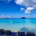 Cruise Ship passengers enjoying a day at the beach on the private island with a cruise ship anchored in the background