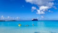 Cruise Ship passengers enjoying a day at the beach on the private island with a cruise ship anchored in the background