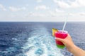 Cruise ship wake or trail on ocean surface with hand holding a glass with cocktail and straw Royalty Free Stock Photo