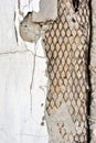 Crumbling painted in white concrete wall with rusty mesh inside