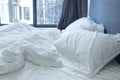 Crumpled bed with white bed linens, sheet, pillows, blanket, grey curtains and window. Royalty Free Stock Photo