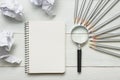 Crumpled paper balls, magnifying glass, pencils and notebook with blank white sheet on wooden table. Creativity crisis Royalty Free Stock Photo