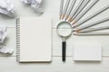 Crumpled paper balls, magnifying glass, pencils and notebook with blank white sheet on wooden table. Creativity crisis Royalty Free Stock Photo