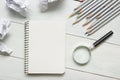 Crumpled paper balls, magnifying glass, pencils and notebook with blank white sheet on wooden table. Creativity crisis Royalty Free Stock Photo