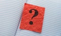 A crumpled red paper note with a question mark on it lying in an open notebook Royalty Free Stock Photo
