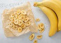 Crunchy dried banana chips on baking paper with bio fresh bananas on light background.Top view Royalty Free Stock Photo