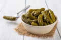 Crunchy pickled cornichons in a beige ceramic bowl and one on a fork on a white wood table. Whole green gherkins marinated with Royalty Free Stock Photo