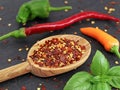 crushed dried chili flakes on wooden cooking spoon with fresh different colored chillies on black slate board Royalty Free Stock Photo