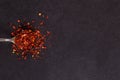 Crushed dried chili peppers in an iron spoon scattered on a black background. Concept, copy space