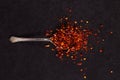 Crushed dried chili peppers in an iron spoon scattered on a black background. Concept, copy space