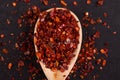 Crushed dried chili peppers in a wooden spoon scattered on a black background. Concept, copy space