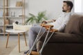Young man with injured leg sitting at home on sofa in rehabilitation with his crutches Royalty Free Stock Photo