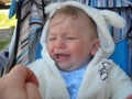 Crying baby. A lovely little boy in a white overalls is sitting in a stroller. Children`s whims and grimaces Royalty Free Stock Photo