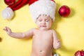 crying baby in a red Santa hat with balls on the New year tree. Beautiful little celebrates Christmas. holidays.