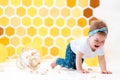 A crying, dirty baby crawls away from a broken cake lying on the floor. In the background is a pattern of yellow honeycombs and Royalty Free Stock Photo