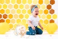 A crying dirty toddler sits next to a broken cake that has fallen to the floor. In the background is a pattern of yellow