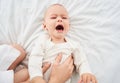 A crying newborn boy in a white bodysuit on a bed Royalty Free Stock Photo