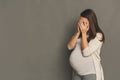 Crying pregnant woman, gray studio background