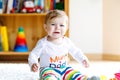 Crying sad baby girl playing with educational toys in nursery. hysteric healthy child having fun with colorful different Royalty Free Stock Photo