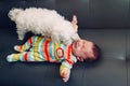 Crying screaming Caucasian baby girl boy lying on bed couch with white dog by his side.