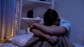Crying teenager sitting alone in evening bedroom, bullying victim, problems