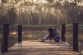 Crying woman hugging her knees on an old wooden bridge jutting out into a pond in nature. Lonely sad woman