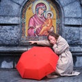 Crying woman with a red umbrella at the Christian icon of the mother of God