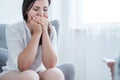 Crying young woman covering her mouth with hands while sitting in a bright room. Empty space in the background Royalty Free Stock Photo