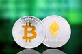 Cryptocurrency Bitcoin and Ethereum silver coins with gold symbols on a green digital background.