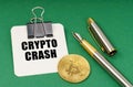 On a green surface, a bitcoin coin, a pen and a sheet of paper with the inscription - Crypto crash