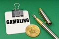 On a green surface, a bitcoin coin, a pen and a sheet of paper with the inscription - Gambling