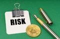 On a green surface, a bitcoin coin, a pen and a sheet of paper with the inscription - Risk