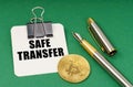 On a green surface, a bitcoin coin, a pen and a sheet of paper with the inscription - safe transfer