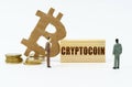 On a white surface, the bitcoin symbol, human figures and a wooden plate with the inscription - Cryptocoin