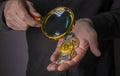 Cryptocurrency coins in male hand with magnifier, closeup. Pile of bitcoin and other crypto currency