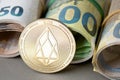 Cryptocurrency EOS golden coin on the background of rolled euro bills. Royalty Free Stock Photo