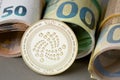 Cryptocurrency IOTA golden coin on the background of rolled euro bills. Royalty Free Stock Photo