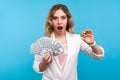 Cryptocurrency. Portrait of surprised charming woman holding physical golden bitcoin and dollars. studio shot, blue background