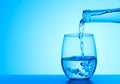 Crystal clear water pouring into the glass on a blue background with copy space. Royalty Free Stock Photo