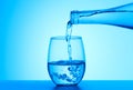 Crystal clear water pouring into the glass on a blue background. Royalty Free Stock Photo