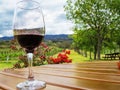 Crystal cup with wine on wooden table with mountains, trees, vineyards and flowers background