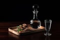 Crystal decanter or carafe with a glass full of vodka and tasty appetizer bruschetta with bacon and pickles on wooden board,