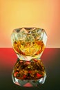Crystal goblet with elite whiskey and ice cubes on a gradient background with reflection