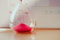 Crystal hourglass with red sand on calendar concept for time slipping away for important appointment date.