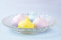 Crystal plate with four small yellow, pink and blue meringues on a pale blue background. Sweet snack concept
